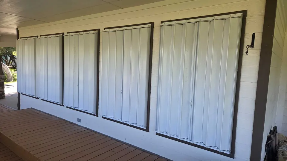 Five white accordion shutters closed across a row of porch windows framed in dark trim