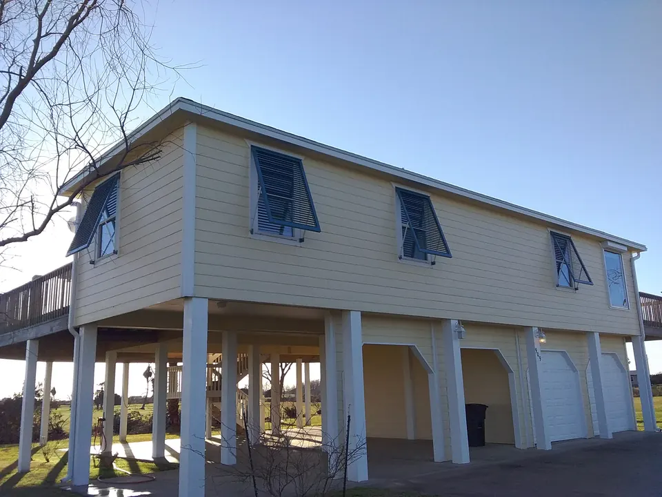 Blue Bahama shutters on a cream house raised on pilings on Bolivar Peninsula