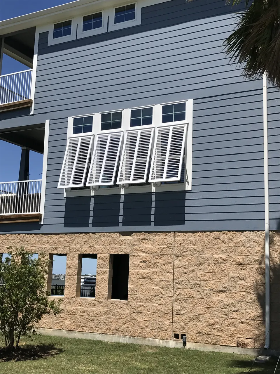 White Bahama shutters over a row of windows on a blue two-story home in the Clear Lake area
