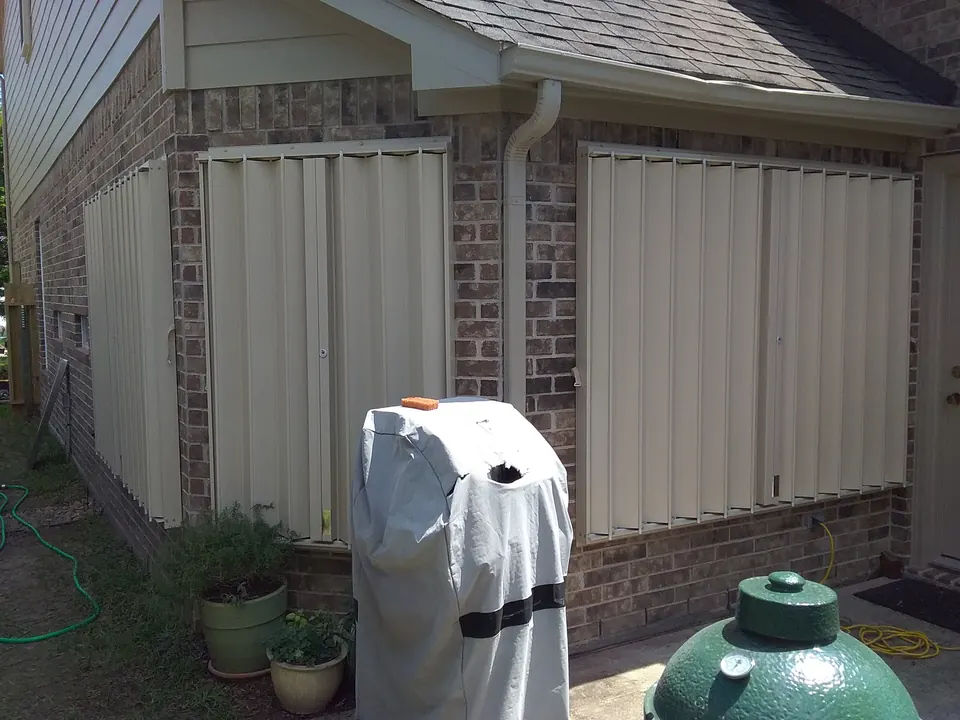 Accordion shutters closed over the windows of a brick and siding home in League City