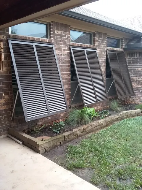 Bronze Bahama shutters propped open over three windows on a brick home in League City