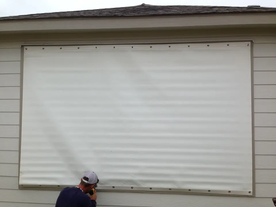Installer fastening a hurricane fabric panel over a window in League City