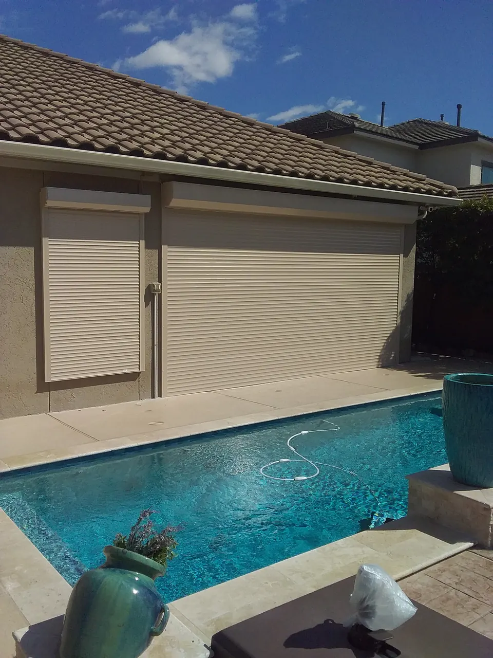 Roll-down shutters closed over the back of a tile-roof home beside a pool in League City