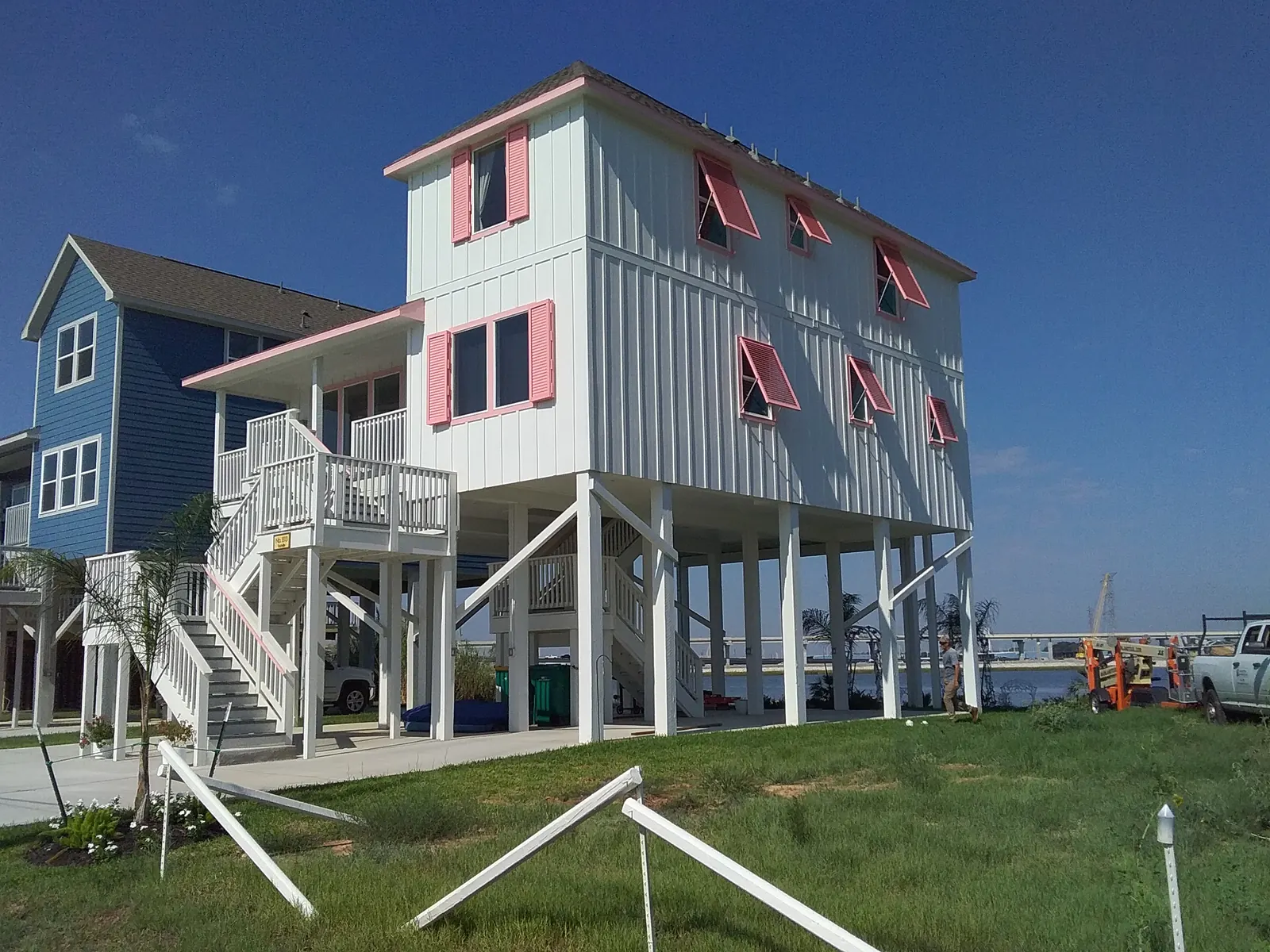 Coral pink Bahama shutters on a white house on stilts by the water in Seabrook