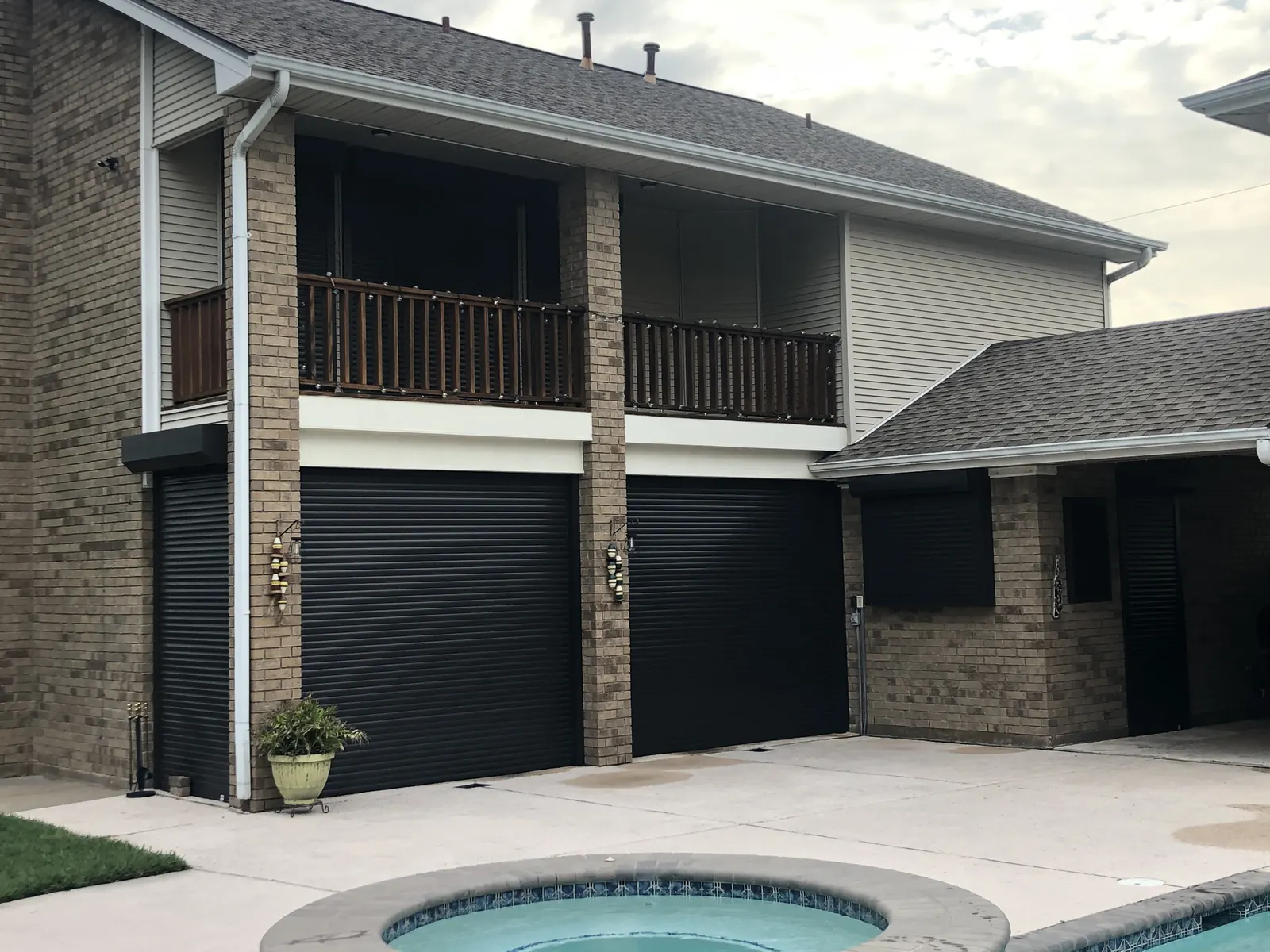 Black roll-down shutters closed across the ground floor of a two-story brick home by a pool in Texas City
