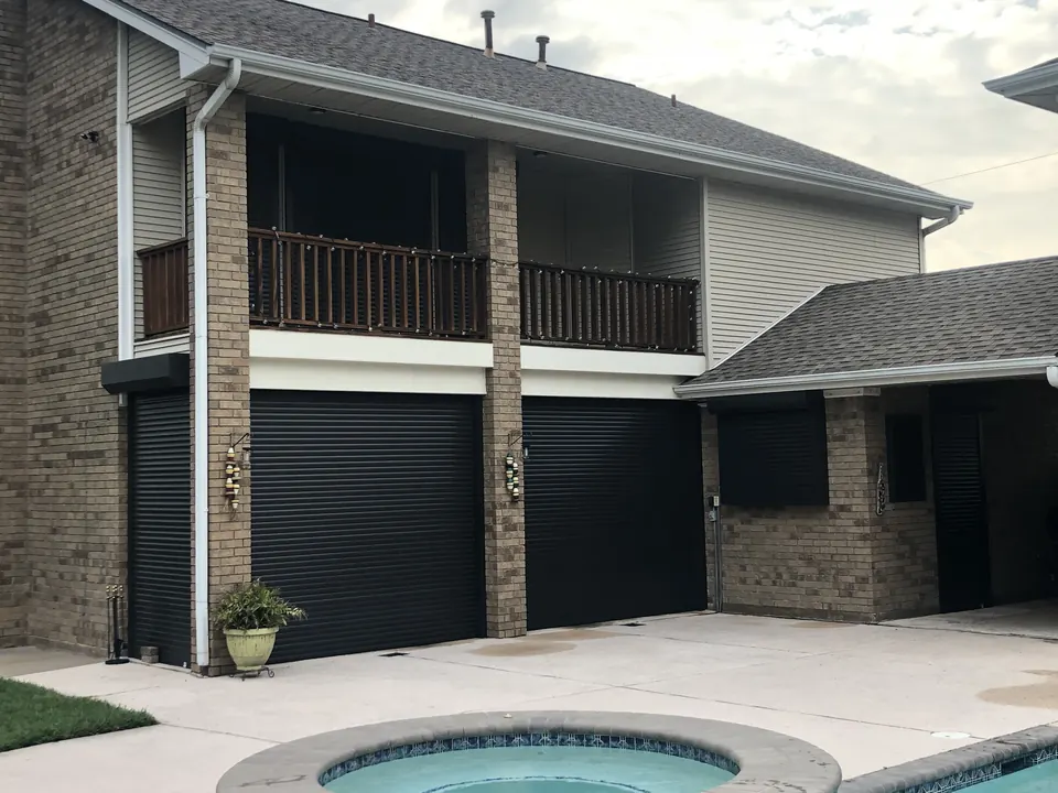 Black roll-down shutters closed across the ground floor of a two-story brick home by a pool in Texas City