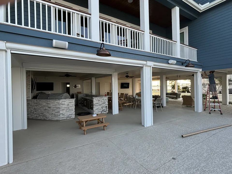 Motorized screen tracks around the ground-floor outdoor kitchen of a raised home in Texas City