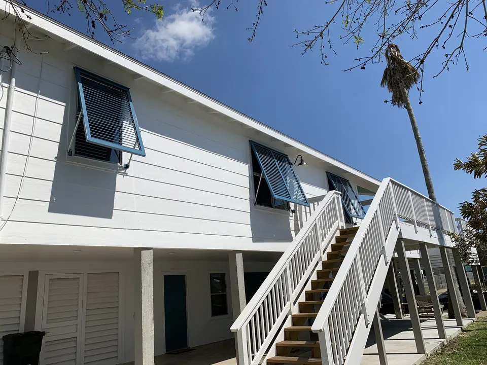 Blue Bahama shutters propped open on a white raised house with a long front stair