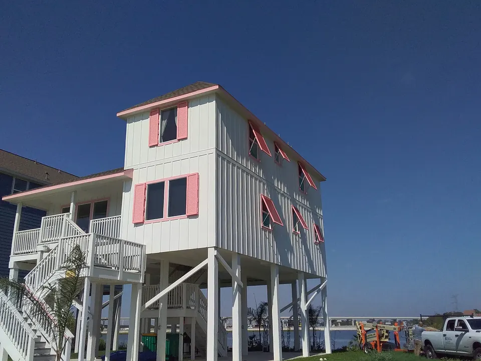 Coral pink Bahama shutters propped open on a tall white board-and-batten raised beach house