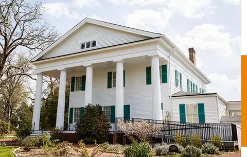 White Greek Revival home with dark green colonial shutters