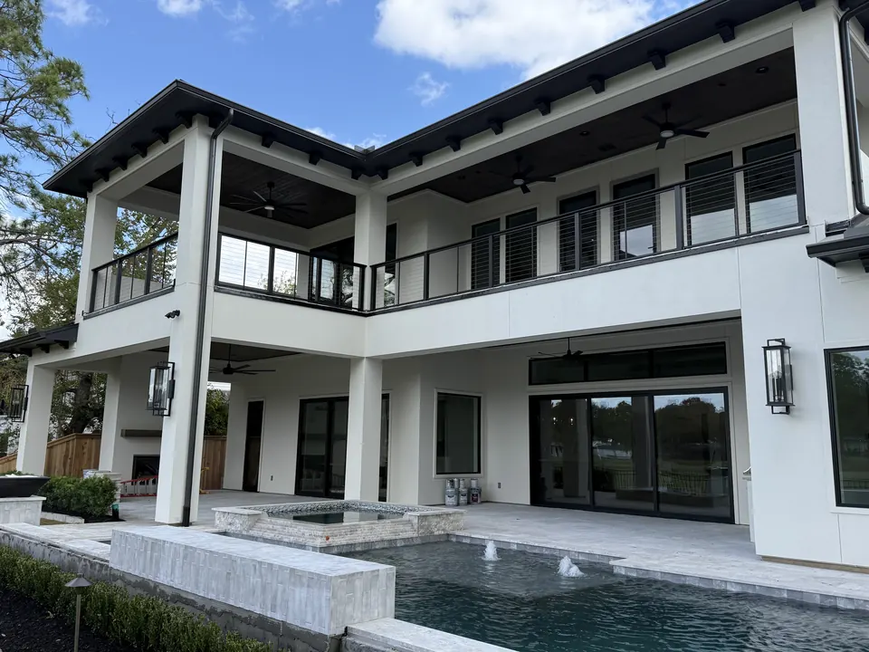 Modern white home with black cable railings on second-floor balconies above a pool