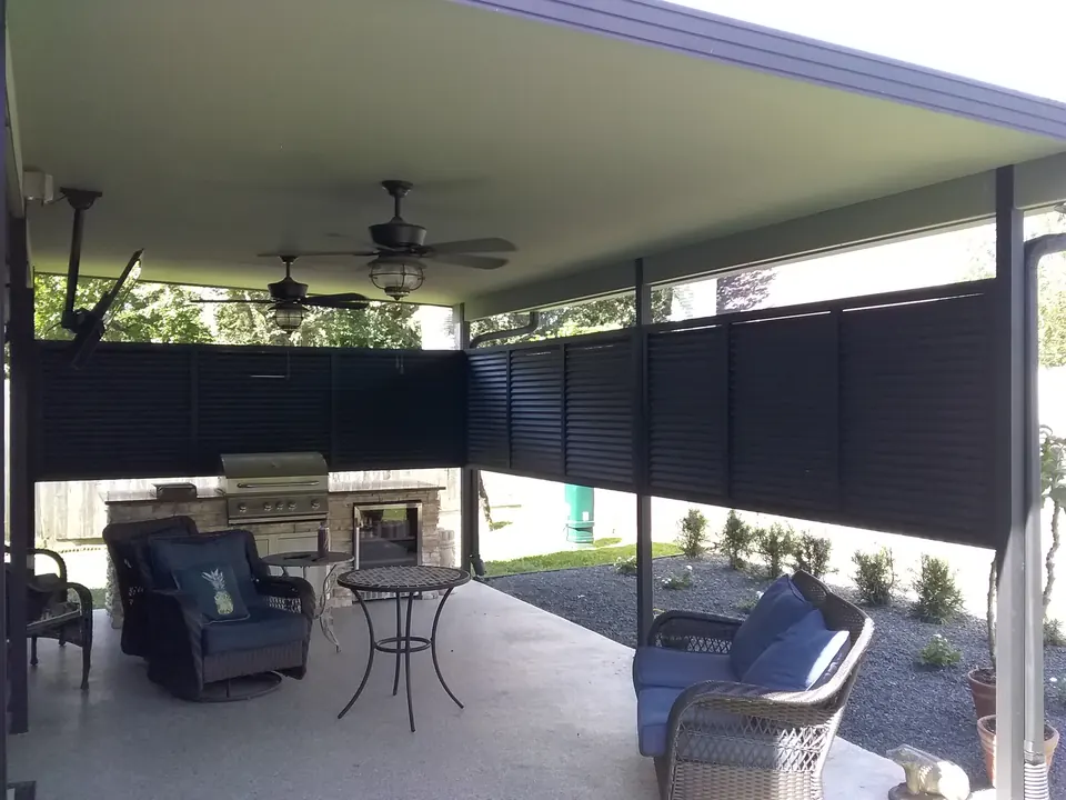 Covered patio enclosed by black louvered privacy panels around an outdoor kitchen and seating