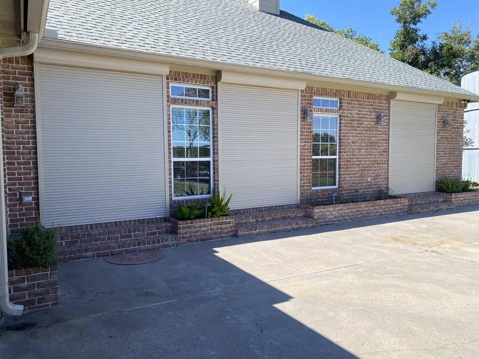 The same Brazoria County ranch with almond roll-down shutters closed over all three French doors