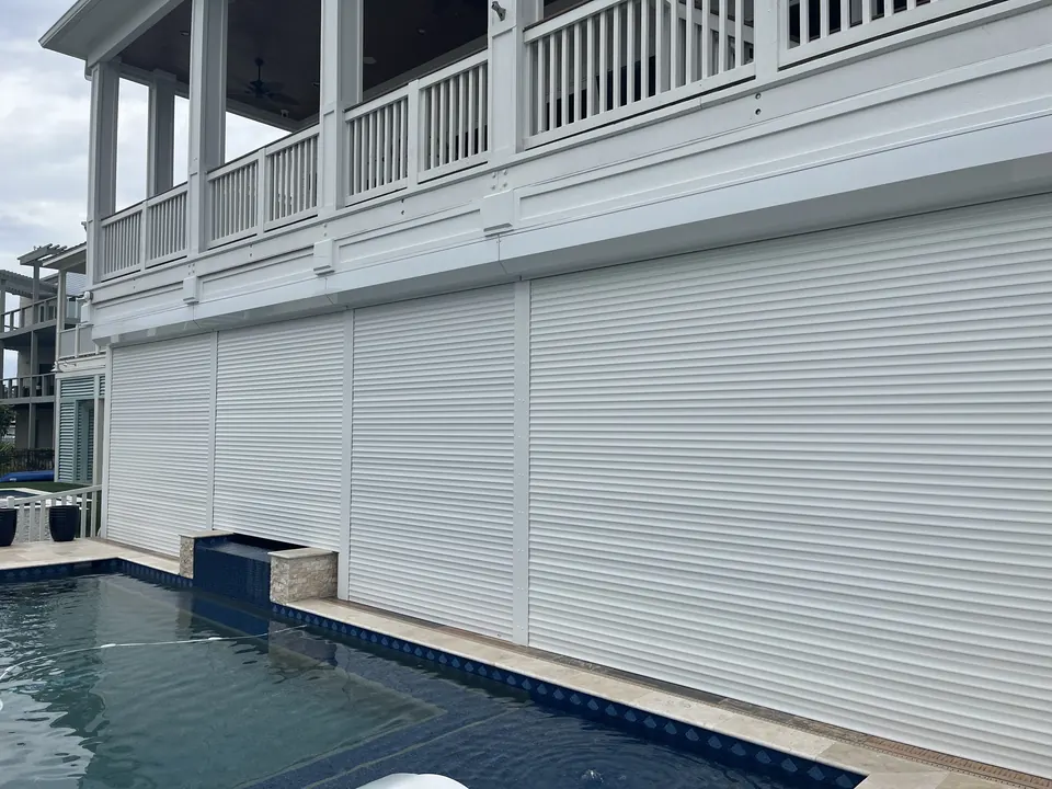 White roll-down shutters closed across the ground floor of a raised home beside a pool
