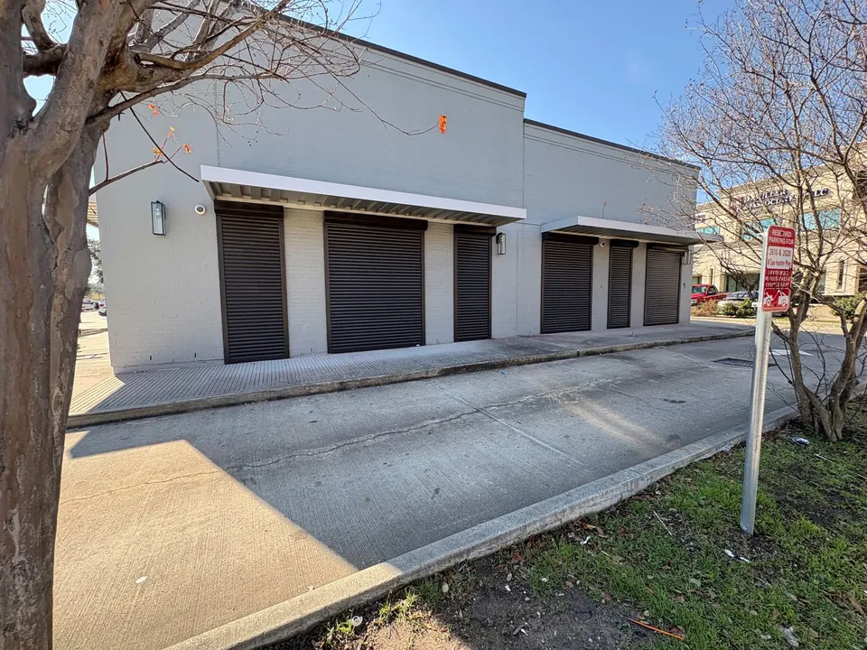 Bronze roll-down shutters closed over storefront windows on a gray brick retail building