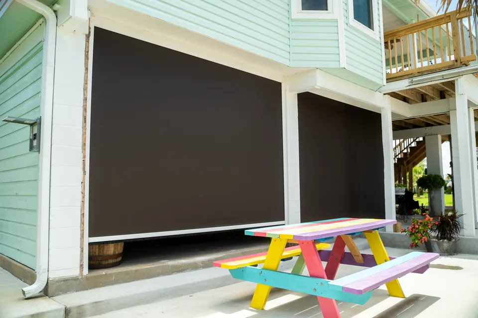 Mint-green raised home with brown screens lowered over ground-level openings
