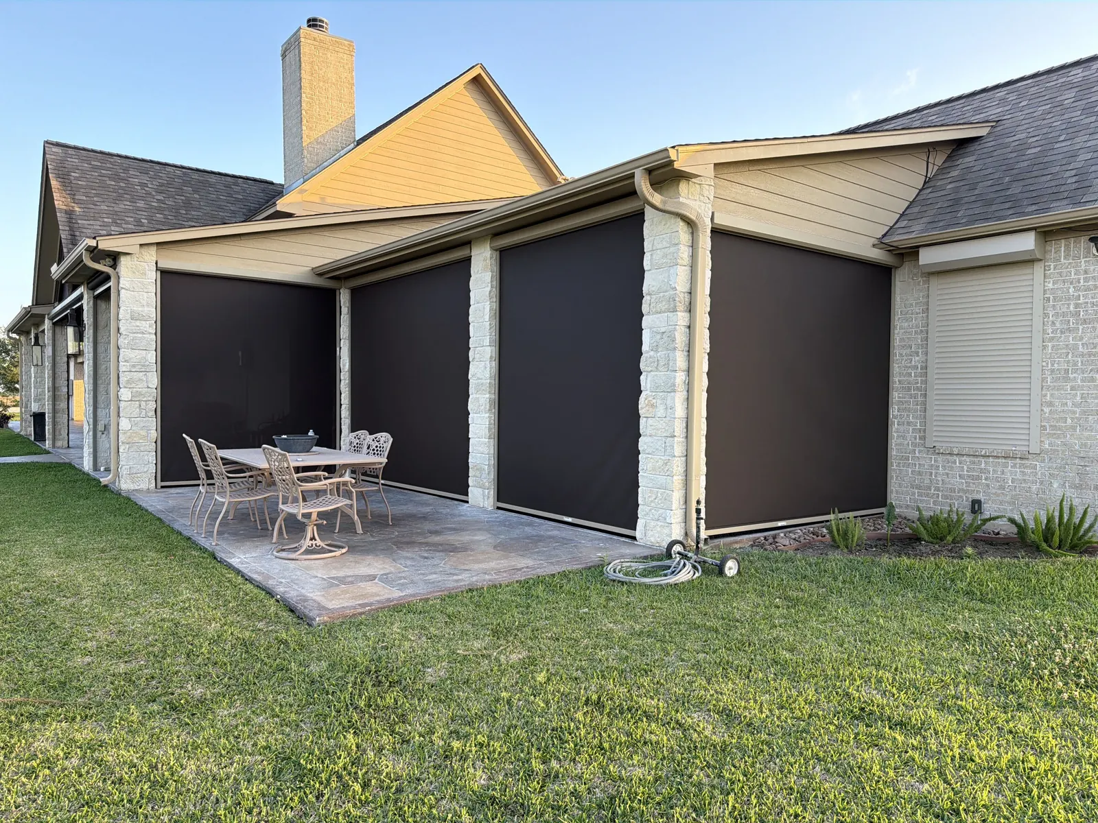 Stone-column patio with dark motorized screens lowered on three sides around a dining set