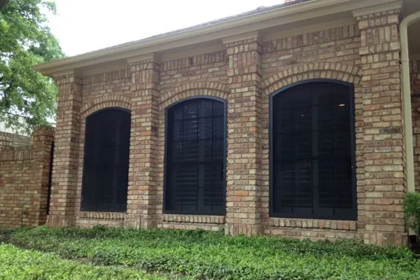 Dark TAPCO screens fitted to the arched windows of a brick home